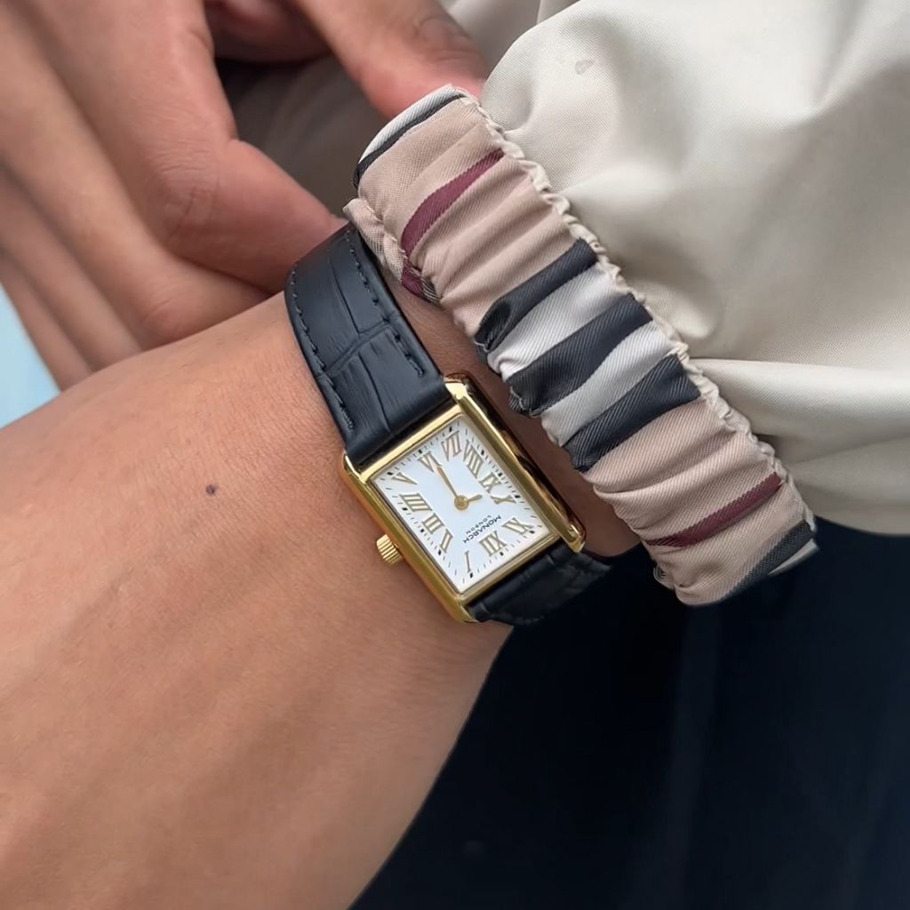 Person wearing a Gold Monarch Timepiece with a striped jacket cuff on a plain background.