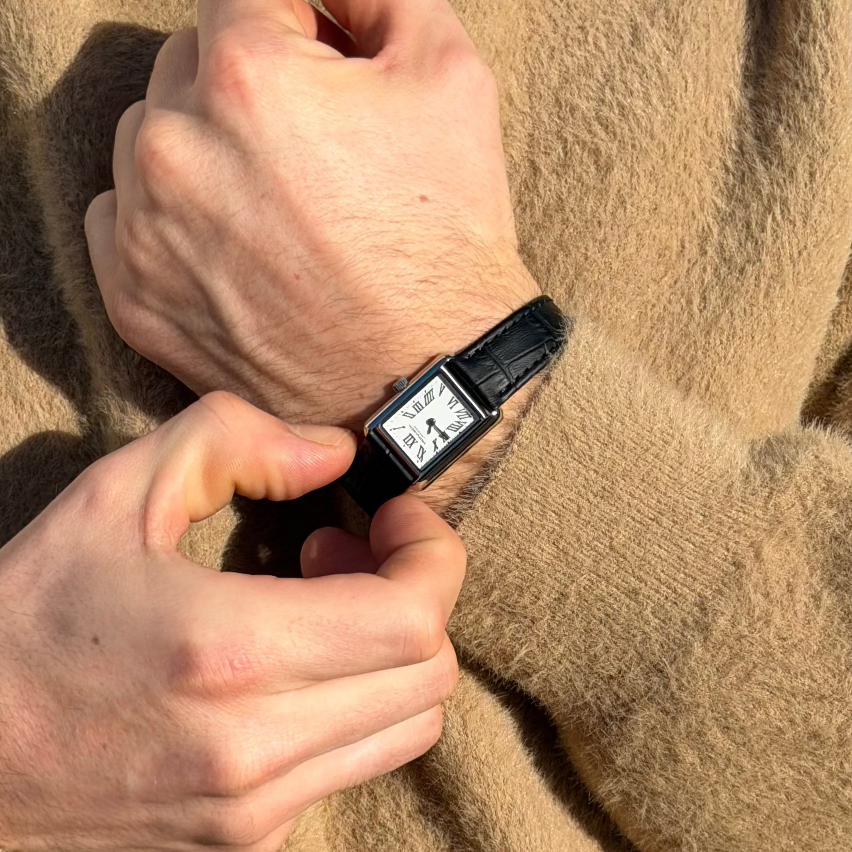 Person wearing a beige sweater holding a black smartwatch with a digital display.